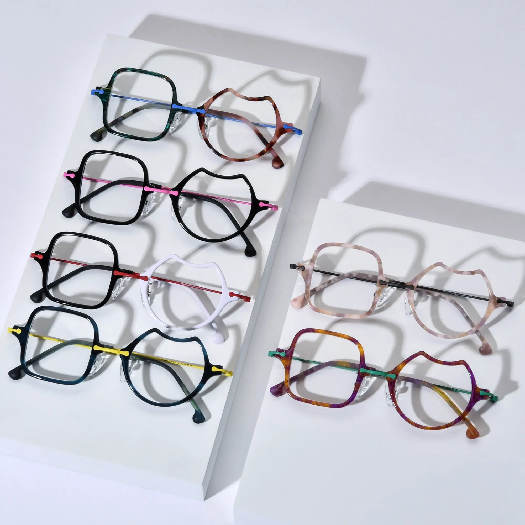 Top-down view of all VoyueLens™ VL185842 Abstract Harmony Eyeglasses color variants including Ocean Brick, Frosted Crimson, Shell Pink, Jungle Carnival, Electric Olive, and Neon Bloom arranged on display platforms.